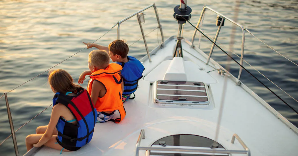 Family boating in Coastal Virginia as kids point toward the sunset from a sailboat.